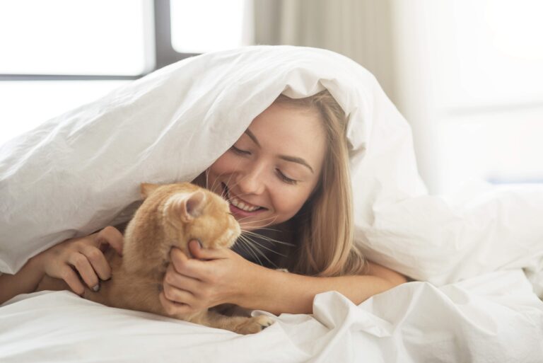 Surround yourself with everything you love. Beautiful girl plays with a cat on the bed.